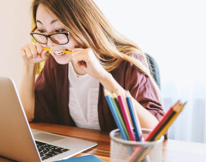 woman biting pencil while sitting on chair in front of computer during daytime
